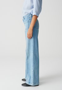 Light blue wide-leg jeans made of denim, featuring a high waist and subtle stitching. Paired with black heeled boots for contrast.