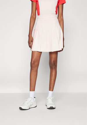 Falda plisada de color rosa pálido con una cintura alta y detalles de costura sutiles, combinada con zapatos blancos y calcetines tobilleros.