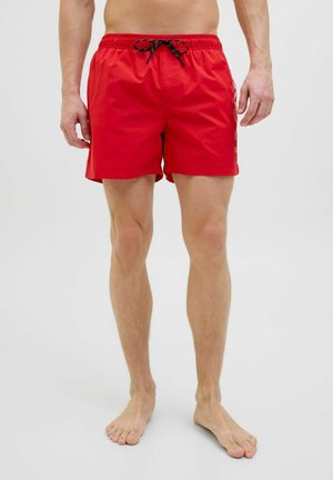 Red swim shorts made of lightweight fabric, featuring an elastic waistband with a black drawstring and side pockets.