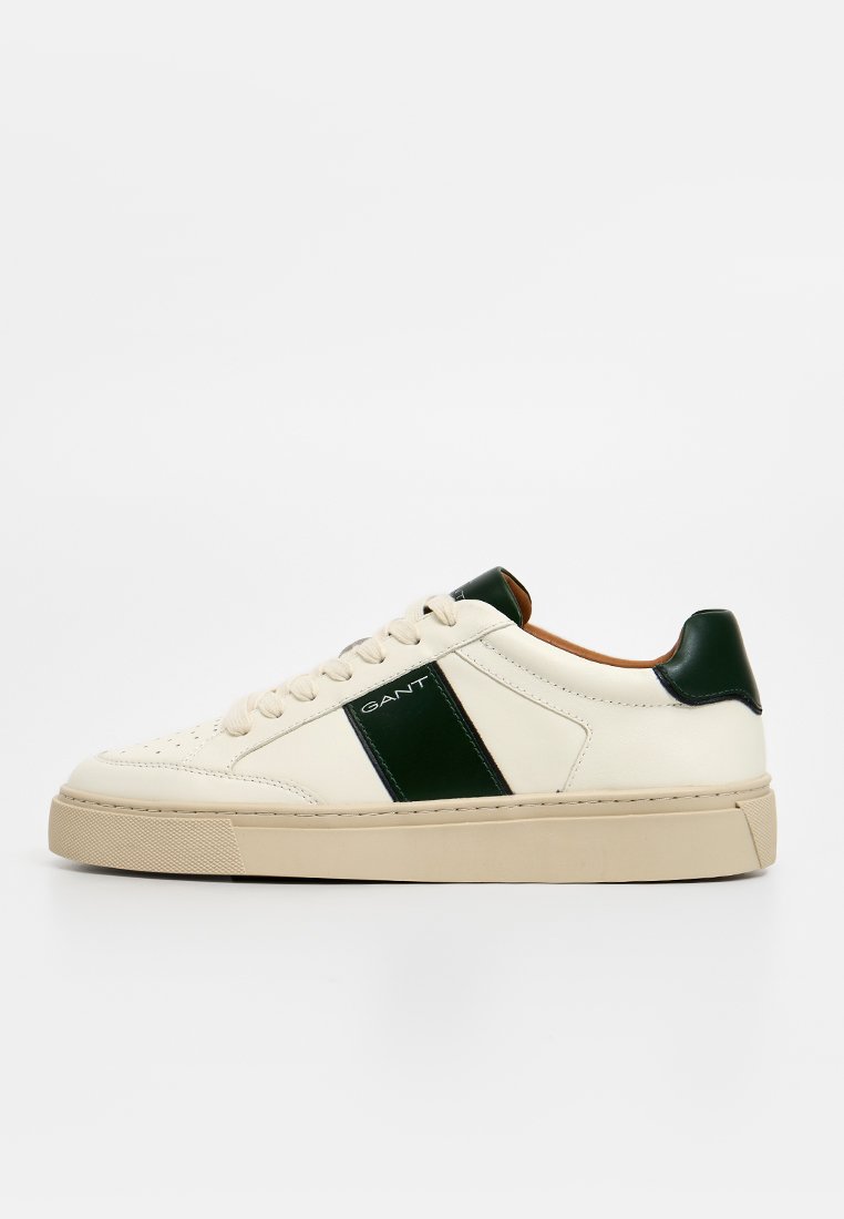 Zapatillas de cuero blanco con una franja de acento verde, suela de goma beige, punta redonda y cierre de cordones en la parte frontal. Detalle de marca en el lateral.