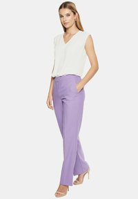Biała bezrękawnikowa bluzka z dekoltem w kształcie litery V, zestawiona z wysokim biustem lawendowymi spodniami z bocznymi kieszeniami, uszytymi z gładkiego materiału.