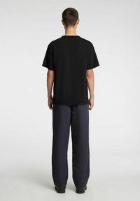 Juoda medvilninė trumpomis rankovėmis marškinėliai, derinami su laisvo kirpimo tamsiai mėlynomis kelnėmis. Aprangoje dominuoja minimalus dizainas ir laisva siluetas.