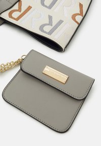 Liten grå läderväska med guldkedja och guld "River Island"-plakett bredvid en beige tygväska med stora flerfärgade bokstäver.