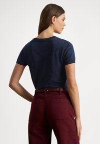 Tengerészkék rövid ujjú pulóver mintás kialakítással és kerek nyakkivágással, bordó magasderekú nadrággal, melyen hátsó zsebek és övhurkok találhatók.