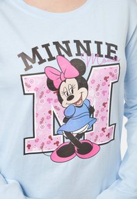 Camicia a maniche lunghe azzurro chiaro con una grafica di Minnie Mouse in un vestito blu, con un fiocco rosa e dettagli floreali attorno al disegno della "M".