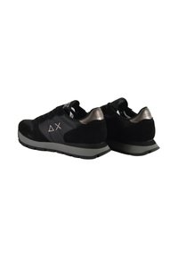 Un paio di scarpe sneakers basse nere con suole grigie, dettagli metallici sul tallone e simboli bianchi a forma di triangolo e croce sui lati su sfondo bianco.