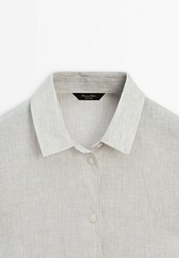 Chemise en tissu côtelé beige clair avec un col classique et des boutons, montrant la partie supérieure y compris l'étiquette à l'intérieur du col.
