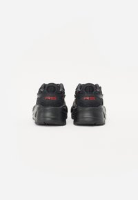 Black athletic shoes featuring a textured design and red accents. The upper has a mix of fabric and synthetic materials for support.