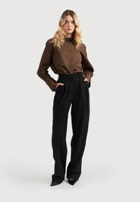 Hnedé pruhované košeľové tričko s dlhými rukávmi, v súlade s čiernymi nohavicami s vysokým pásom. Model stojí s rukami v vreckách, vystúpené čierne lodičky.