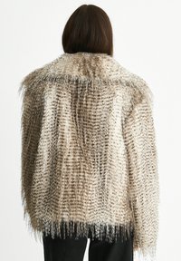 Person with long brown hair wearing a brown and beige speckled faux fur jacket, facing away against a white background.