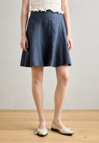Navy blue linen A-line skirt with a fitted waistband and textured fabric, paired with cream flats featuring a bow detail.