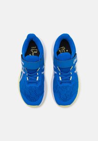 Baskets de sport bleues avec une tige en maille, semelle blanche, accents jaunes, sangle réglable et surface texturée.