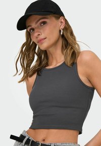 Grå ribbet crop top med rund halsudskæring, parret med en sort kasket. Modellen har langt bølget hår og sølvfarvede hoop øreringe.