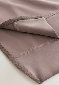Blødt, strækbart stof i dæmpet mauve med en glat tekstur. Har flade sømme og en fiskebensdetalje langs kanten.