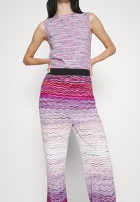 Haut sans manches en tissu rayé multicolore associé à un pantalon à motif en zigzag, passant du violet au blanc avec une ceinture noire.