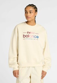 Sweatshirt de couleur crème en tissu doux, arborant un graphique sur le devant avec "new balance" en texte rose et bleu, col rond et poignets côtelés.