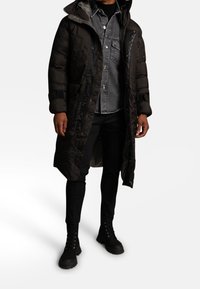 Czarna pikowana kurtka o długim fasonie, z zamkiem błyskawicznym z przodu, dwoma bocznymi kieszeniami i kapturem. Pod spodem szara koszula dżinsowa. Czarne spodnie i buty.