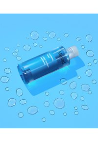 Bottiglia di plastica blu del Tonico Purificante Murad con un tappo bianco, circondata da gocce d'acqua su uno sfondo blu abbinato.