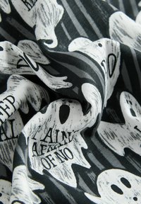 Black and white fabric with printed ghost shapes and partially visible Halloween-themed text, shown in a close-up with folds.
