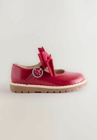 Soulier Mary Jane en cuir verni rouge avec une semelle beige épaisse, une bride à boucle argentée et un grand nœud décoratif sur le dessus.