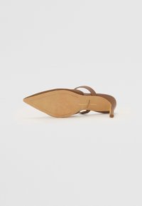 Sandale à talon aigu en cuir beige avec un talon fin et des lanières étroites. Semelle intérieure texturée et coutures décoratives le long de la semelle.