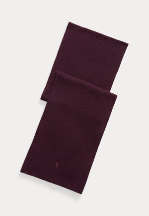 Tmavofialový pletený šál zložený na plochu s jemne vyšitým logom blízko jedného konca na svetlom pozadí.