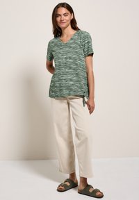 Groene, kortarmige V-hals top met een zebra-streep patroon, gecombineerd met lichte brede broek en donkergroene sandalen.