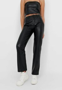Hoge taille zwarte neplederen broek met een rechte pijpdesign, voorzien van voorzakken en zichtbare naaddetails, gecombineerd met witte sneakers.