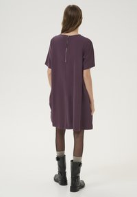 Robes violettes à manches courtes avec un col rond, dotées d'une fermeture éclair au dos et d'une coupe ample, associées à des bottes noires et des chaussettes grises montantes.
