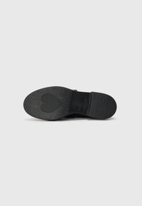 Suola nera di scarpa con superficie testurizzata e design a forma di cuore vicino al tallone. Presenta un'impronta del marchio e un tallone arrotondato.