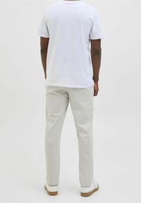 Bílá bavlněná trička s krátkým rukávem, spárovaná se světle šedými kalhotami a bílými teniskami s hnědou podrážkou. Jednoduchý design, minimální detaily.