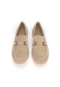 Mocasines de ante color beige con acentos de hebilla plateada y suelas de goma blanca gruesas, mostrados desde una vista superior sobre un fondo blanco.