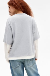Gray short-sleeve T-shirt with a relaxed fit and soft texture, layered over a white long-sleeve shirt, paired with light-wash jeans.