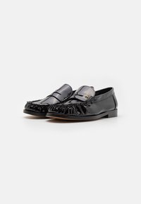 Mustad lakknahast loafers, millel on pleekitud disain ja dekoratiivne metallist detail. Lame tald ja ümar varvas. Sile tekstuur, ametlik stiil.