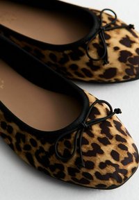 Leopard print flat shoes with a textured fabric upper, black trim around the opening, and a decorative bow on the front.