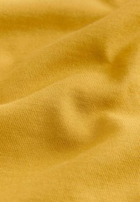 Gros plan d'un tissu jaune texturé avec un motif tricot visible et des plis doux créant des ombres et des lumières.