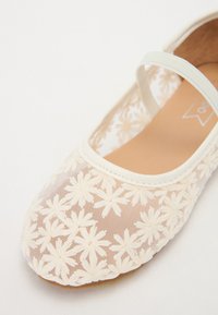 Ballerina bianca con tomaia in rete traslucida, impreziosita da ricami floreali. Include una sottile cinghia sopra il dorso del piede.