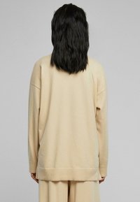 Beige isoitu neule, jossa on pyöreä pääntie, pitkät hihat ja yksinkertainen ribbaushelma. Pehmeä kangas, jolla on sileä pinta ja rento muotoilu.