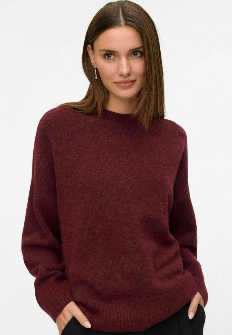 Burgundy stickad tröja med rund halsringning, sänkta axlar och ribbade muddarna och nederkant. Mjuk textur, avslappnad passform.