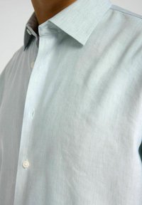 Camicia azzurro chiaro con bottoni, realizzata in tessuto testurizzato, con colletto classico e un singolo bottone sulla patta.