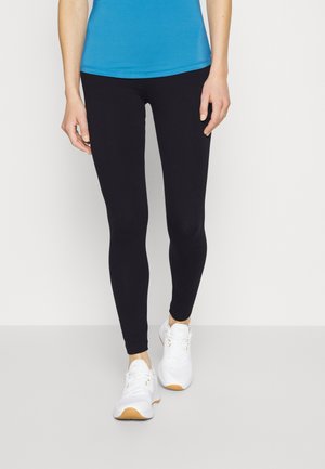 Leggings neri con una texture liscia, caratterizzati da un design aderente che arriva fino alle caviglie. Abbinati a sneakers bianche e a un top blu.