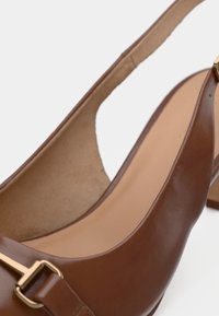 Chaussure à talon haut en cuir marron avec un design à bride arrière, ornée d'une boucle dorée et d'une texture lisse à l'extérieur.