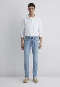 Light blue jeans, fitted with five pockets, combined with a white button-up shirt, featuring a chest pocket, lightweight fabric, and rolled sleeves.