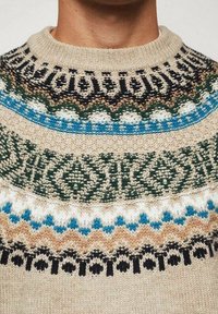 Pull en tricot beige avec un col rond et de délicats motifs multicolores en vert, bleu, noir et blanc autour de l'emmanchure.
