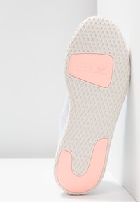 Vit sneakersula med ett texturerat mönster och en rosa accent. Har en formar logo och en distinkt häldesign med en utskuren form.