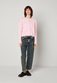 Rožinė pūkuota kardiganas su ilgomis rankovėmis ir mygtukų uždarymu, derinamas su aukšto juosmens išblukusiais džinsais ir juodais platforminiais bateliais.