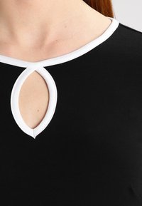 Top nero con scollo rotondo, rifinito con un bordo bianco e un piccolo dettaglio a taglio al centro. Tessuto morbido, design aderente.