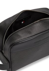 Μαύρο υφασμάτινο δερμάτινο νεσεσέρ με ασημένιο φερμουάρ που είναι μερικώς ανοιχτό, μπροστινή τσέπη και το λογότυπο Tommy Hilfiger ανάγλυφο στην εμπρόσθια πλευρά.