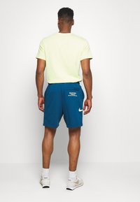 Back view of a person wearing a light green short-sleeve shirt and navy blue shorts with a white Nike logo and pockets.