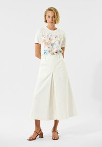 Hvid t-shirt med blomsterprint og korte ærmer, parret med højtaljede, brede cremede bukser. Brune hæle sandaler fuldender outfittet.